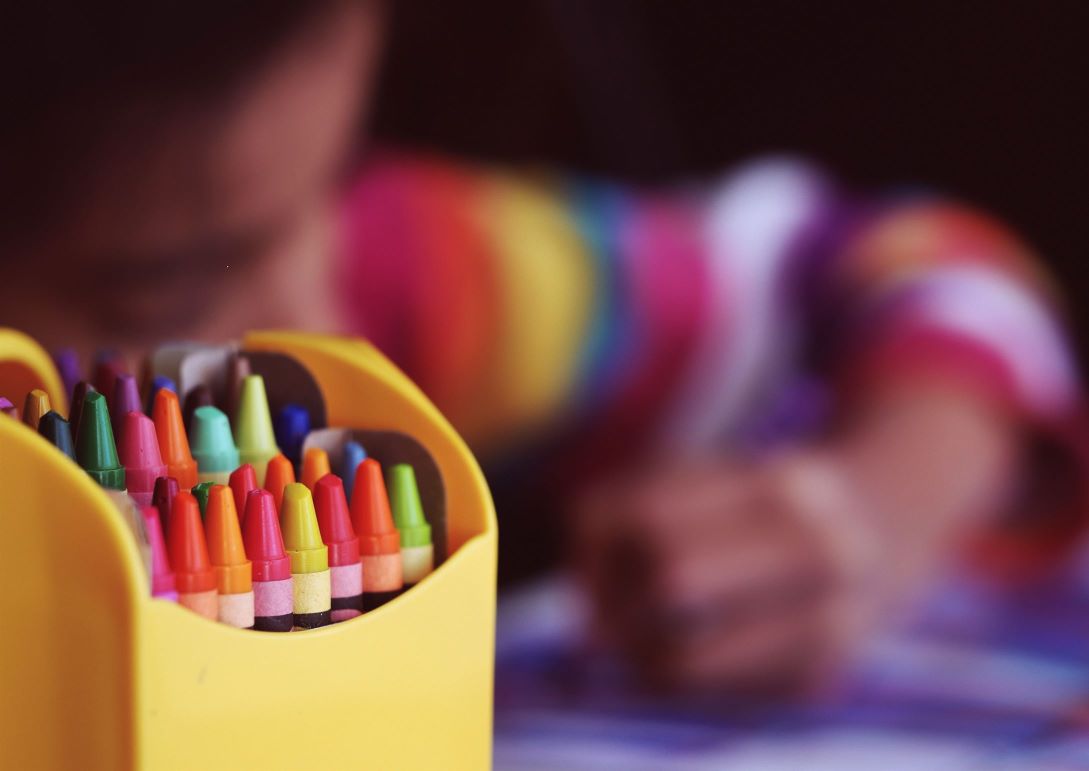 Rainbow crayons with child drawing in background